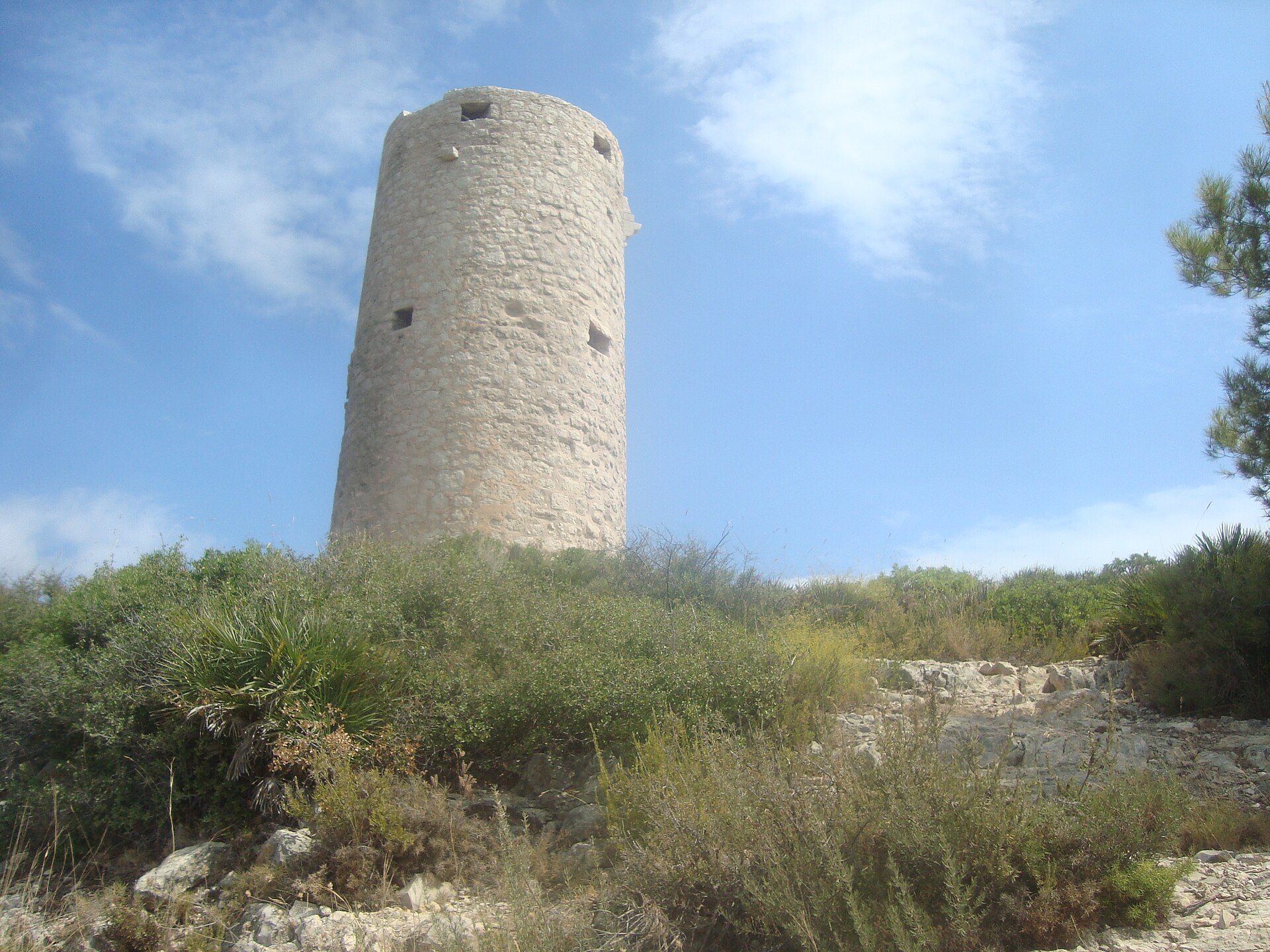 La Torre Badum, torre vigía de piedra sobre un cerro, bajo un cielo azul.